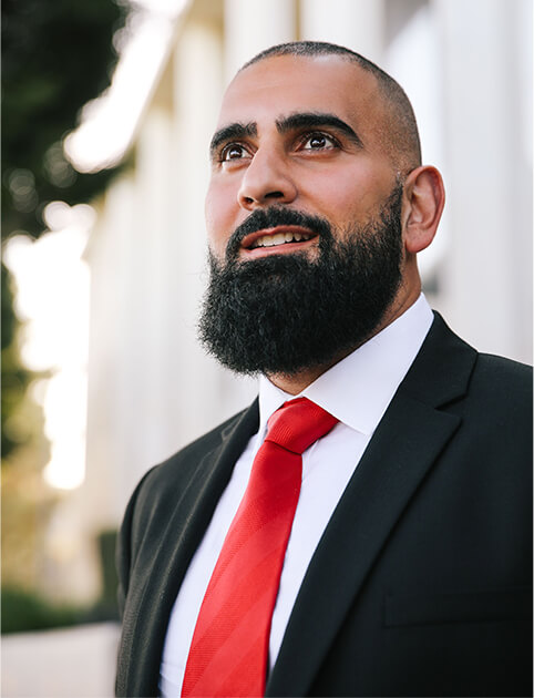 Image of Farshad Dehbozorgi in black suit and red tie looking left off to the distance