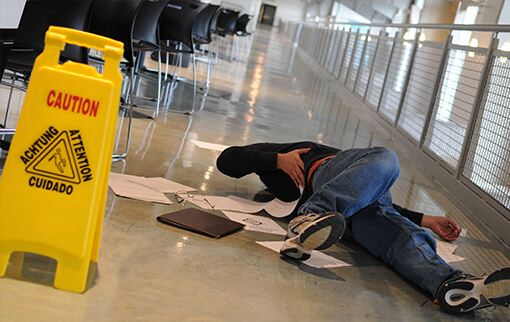 Photo of a man lying on his back on the floor holding his back beside a Caution sign