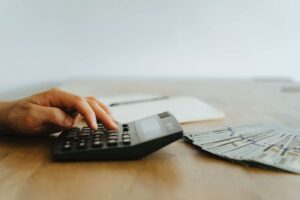 Someone using a calculator with a pile of money spread out over the table