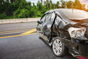 Photo of a car in the middle of a road that has been significant damaged on the back side enough that it is no longer drivable