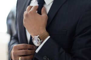 Photo of what appears to be a lawyer between his waist and neck adjusting his tie while wearing an expensive watch