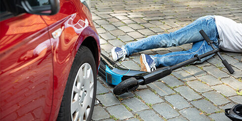 Photo of an electric scooter beside a car with someone on the ground