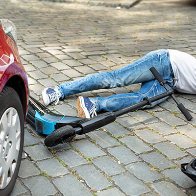 Photo of an electric scooter beside a car with someone on the ground