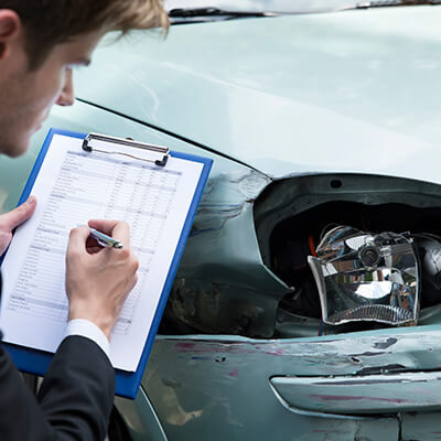 Photo of what appears to be a car insurance auditor checking over the damage of the front of a car
