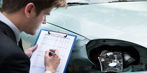 Photo of what appears to be a car insurance auditor checking over the damage of the front of a car